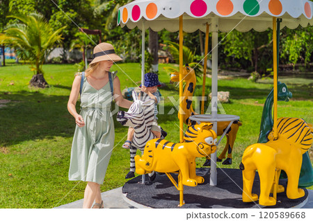 a little boy is a blonde child with mother in an amusement park, riding on a carousel, smiling, rejoicing 120589668