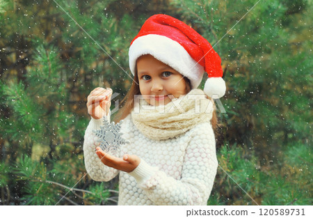 Christmas portrait of happy smiling little girl child in santa red hat with snowflake toy outdoors 120589731