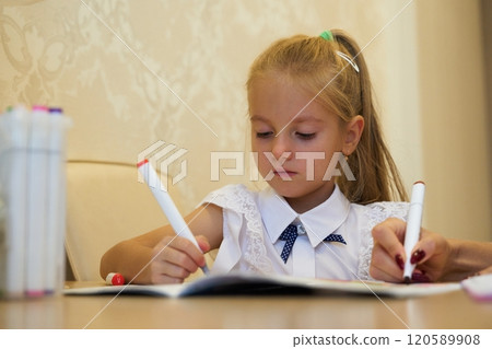 Young girl focused on drawing with colorful markers at a study table 120589908