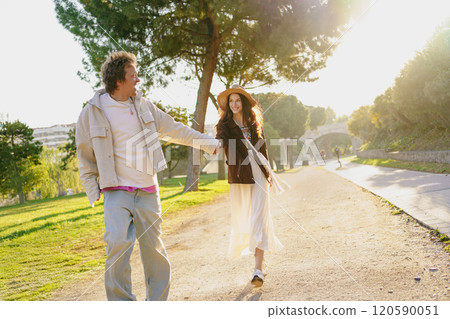 A Couple Walking Hand in Hand Together in a Bright Sunlit Park Full of Vibrant Fun and Love A Couple Walking Hand in Hand Together in a Bright Sunlit Park Full of Vibrant Fun and Love 120590051