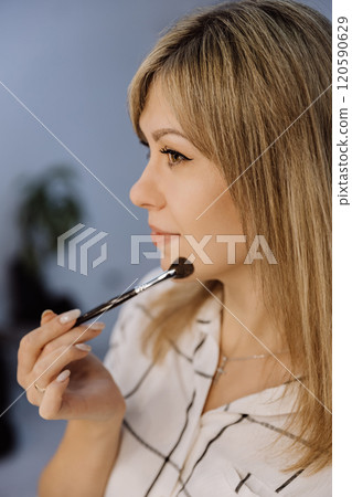 Profile of a woman applying makeup with a brush, showcasing precision and beauty 120590629