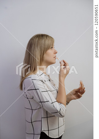 Profile view of a woman applying lip gloss, highlighting elegance and minimalistic beauty Profile view of a woman applying lip gloss, highlighting elegance and minimalistic beauty 120590651