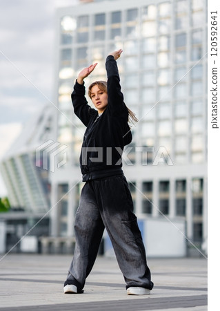 Young woman performing dance moves outdoors in urban setting during daytime 120592641