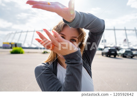 Young woman posing outdoors with hands raised against bright sunlight 120592642