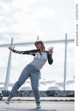 Woman dancing in urban setting with white boats in background under cloudy sky Woman dancing in urban setting with white boats in background under cloudy sky 120592703