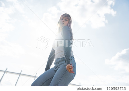 Young woman posing confidently against a bright sky during daytime 120592713