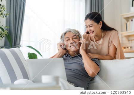 Senior spouses using laptop together sitting on couch at home 120593540