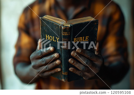 African American man holds an open black holy Bible in his hands. 120595108
