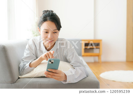 A woman lying on the sofa and looking at her smartphone A woman lying on the sofa and looking at her smartphone 120595239