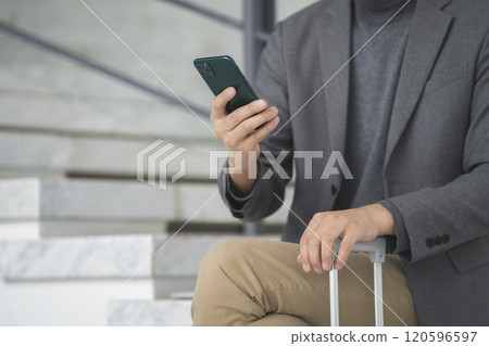 拿著手提箱把手和智慧型手機的一個人的手 120596597