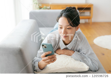A woman lying on the sofa and looking at her smartphone 120596726