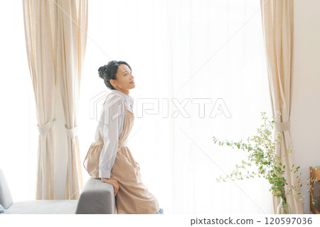 客廳窗邊站著一個穿著圍裙的女人 120597036