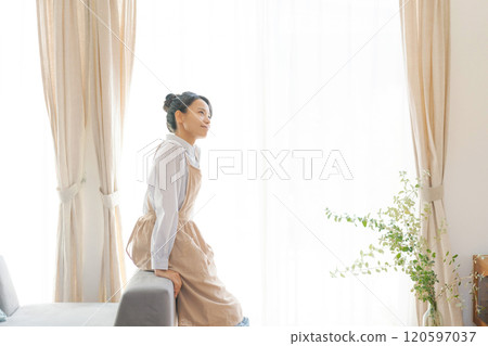 客廳窗邊站著一個穿著圍裙的女人 120597037