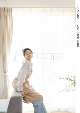 客廳窗邊站著一個穿著圍裙的女人 120597042