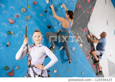 Portrait of sports woman in climbing equipment and safety rope on background of climbing wall Portrait of sports woman in climbing equipment and safety rope on background of climbing wall 120598325