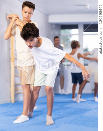 Diligent preteen student twisting his opponent's arm in sports hall 120598443