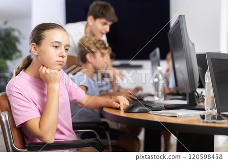 Confused preteen girl sitting at computer table in training room Confused preteen girl sitting at computer table in training room 120598458