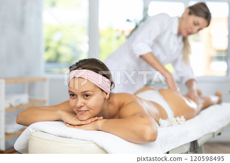 Young woman enjoying massage of thighs and buttocks in spa center 120598495