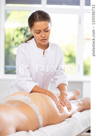 Professional young masseuse performing thigh and butt massage to female client Professional young masseuse performing thigh and butt massage to female client 120598732