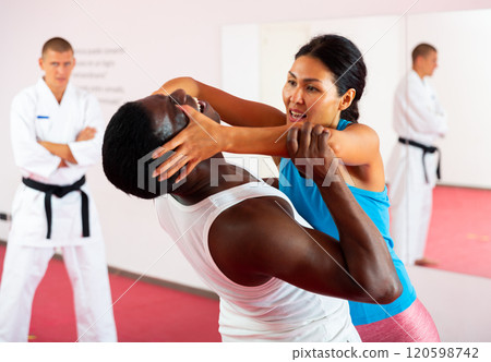 Sportive woman conducts painful reception on the eyes of man in gym. Self defense lessons Sportive woman conducts painful reception on the eyes of man in gym. Self defense lessons 120598742
