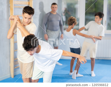 Diligent preteen student twisting his opponent's arm in sports hall Diligent preteen student twisting his opponent's arm in sports hall 120598812