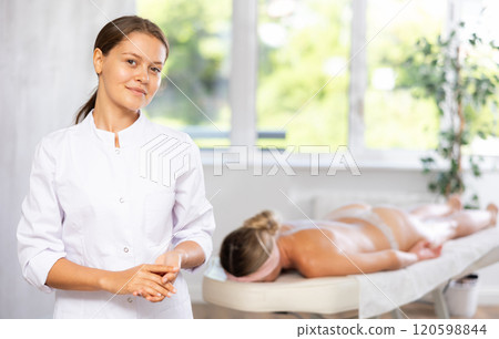 Positive young professional masseuse standing in massage room Positive young professional masseuse standing in massage room 120598844