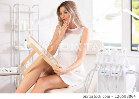 Positive woman examining her face after cosmetic procedure in medical room Positive woman examining her face after cosmetic procedure in medical room 120598864