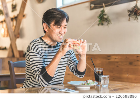 Asian man eating hamburger at cafe or restaurant during lunch break 120598886