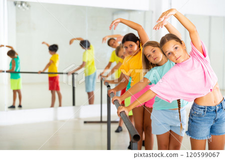 Assiduous preteen girl working near ballet barre during group choreography class Assiduous preteen girl working near ballet barre during group choreography class 120599067