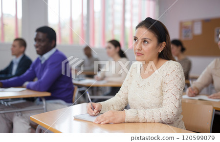Focused young Latina listening to lecture in classroom with group 120599079