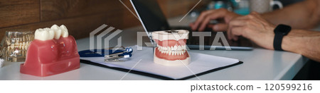 Typing on Laptop near Dental Prostheses and Tools 120599216