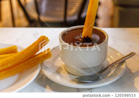 Dipping churros into hot chocolate mug. Churros - traditional spanish dessert 120599553
