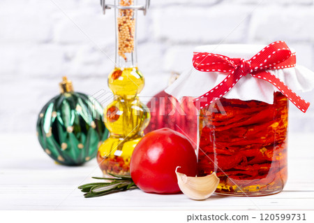 Sundried tomatoes with herbs in a jar for Christmas on a table with ingredients. 120599731
