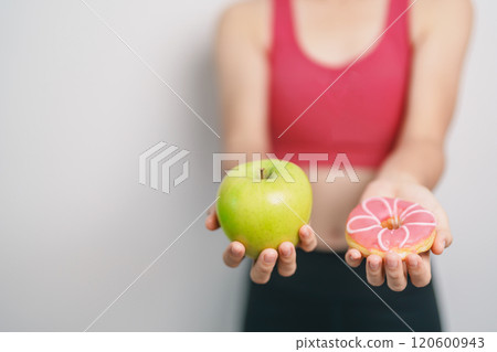 woman hand hold green Apple and donut, female fitness choose between fruit is Healthy and sweet is Unhealthy junk food. Dieting control, Weight loss, Obesity, eating lifestyle and nutrition concept 120600943