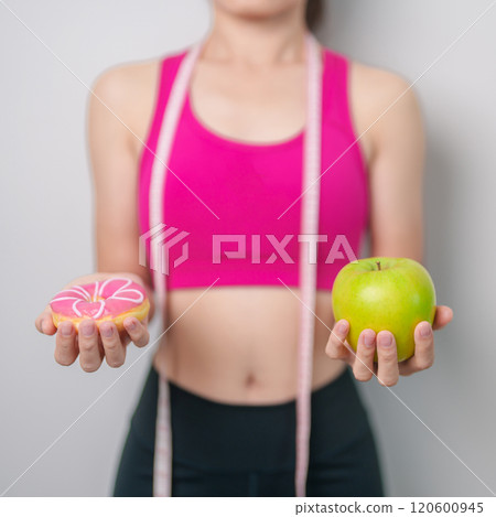 woman hand hold green Apple and donut, female fitness choose between fruit is Healthy and sweet is Unhealthy junk food. Dieting control, Weight loss, Obesity, eating lifestyle and nutrition concept 120600945
