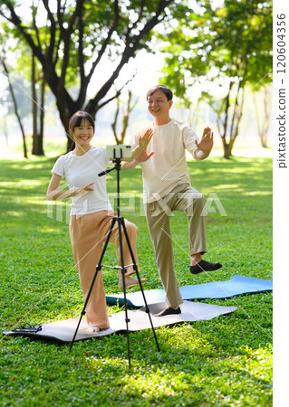 Young woman and middle aged man practicing Tai Chi in a park and recording video online training with mobile phone 120604356