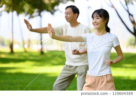 Pretty woman and middle aged man practicing Tai Chi together in scenic park. Mindfulness and health concept 120604389