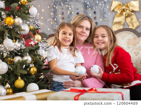 Happy mother with two girls near the Christmas tree in the living room. Christmas Eve, in anticipation of holiday 120604489