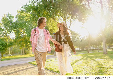 A young couple enjoying a leisurely stroll in a sunlit park, surrounded by natures beauty A young couple enjoying a leisurely stroll in a sunlit park, surrounded by natures beauty 120605647