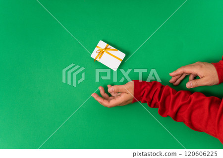 Woman hands holding a white plastic card tied with a yellow ribbon on a bright green background. Suitable for gifting on Christmas, Mother's Day, or special occasions 120606225