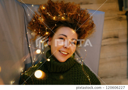 Cozy Christmas and New Year scene with a woman lying on a couch, surrounded by glowing lights. Joyful and festive moment of woman lying on couch, enjoying the holiday glow of Christmas and New Year 120606227