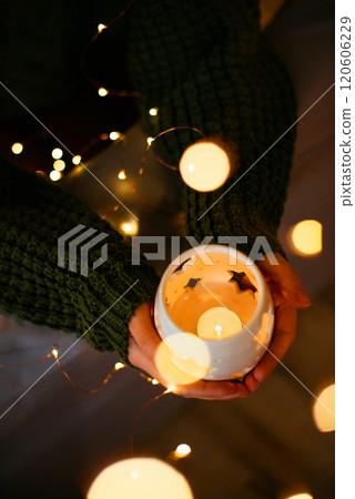 Woman holding a glowing candle lantern with holiday lights, celebrating Christmas and New Year in a serene and festive atmosphere 120606229