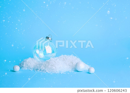 Minimalist Winter Blue Background with Glass Christmas Decoration and Snowflakes, Copy Space. Modern festive background with snow and a shimmering glass ornament for advertising or greetings 120606243