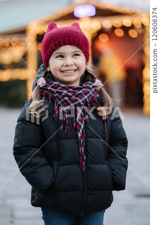 Portrait of adorable little girl standing in front of Christmas lights in old town. Background of bokeh  120606374