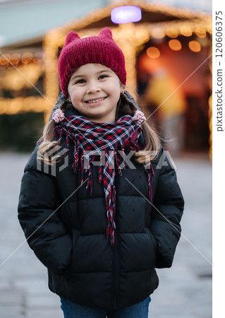 Portrait of adorable little girl standing in front of Christmas lights in old town. Background of bokeh Portrait of adorable little girl standing in front of Christmas lights in old town. Background of bokeh 120606375