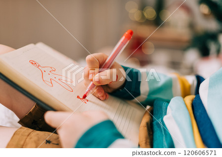 Kid boy in red Santa hat writing the letter and drawing to dear Santa at home. Child wish list. Dreams of a Christmas gifts. Merry Christmas and Happy new year. 120606571