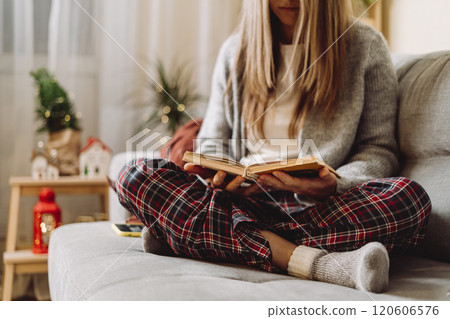 Cozy woman in knitted winter warm socks and sweater with checkered plaid reading a book, during resting on couch at home in Christmas holidays. Domestic life, female indoors Cozy woman in knitted winter warm socks and sweater with checkered plaid reading a book, during resting on couch at home in Christmas holidays. Domestic life, female indoors 120606576