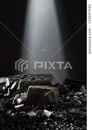 A dark stone block with an empty space, placed on the gravel surface, surrounded by some charcoal blocks and coal pieces. In the dark backdrop with a light like a stage for product showcases. A dark stone block with an empty space, placed on the gravel surface, surrounded by some charcoal blocks and coal pieces. In the dark backdrop with a light like a stage for product showcases. 120607483