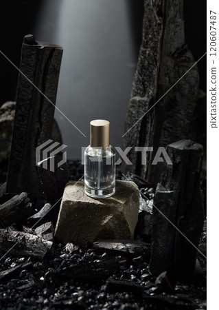 An advertisement photo template in the dark background, high angle, shows a glass bottle containing a transparent liquid placed on a stone block. Charcoal ingredient and gravels surrounded a surface. 120607487