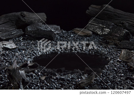 For a charcoal-themed advertising photo template with a dark background, a close-up angle of an oval dark chamber surrounded by charcoal particles, dark gray, and black stones is perfect. For a charcoal-themed advertising photo template with a dark background, a close-up angle of an oval dark chamber surrounded by charcoal particles, dark gray, and black stones is perfect. 120607497